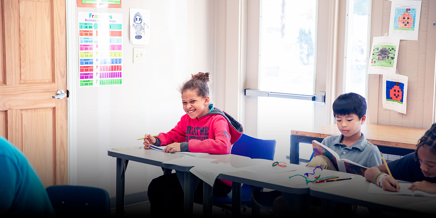 Smiling students working at their desks in a classroom.